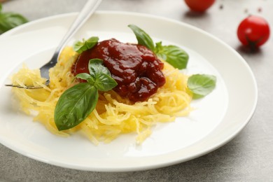 Photo of Tasty spaghetti squash with tomato sauce and basil served on light grey table, closeup