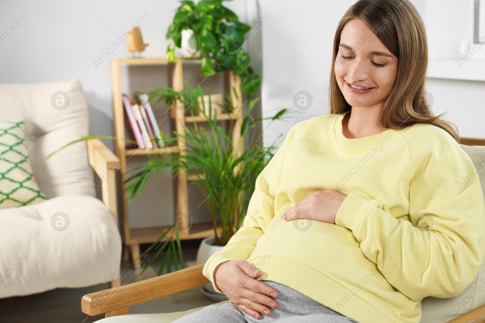 Photo of Happy pregnant woman touching belly in living room