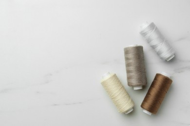 Photo of Sewing threads on white marble table, flat lay. Space for text