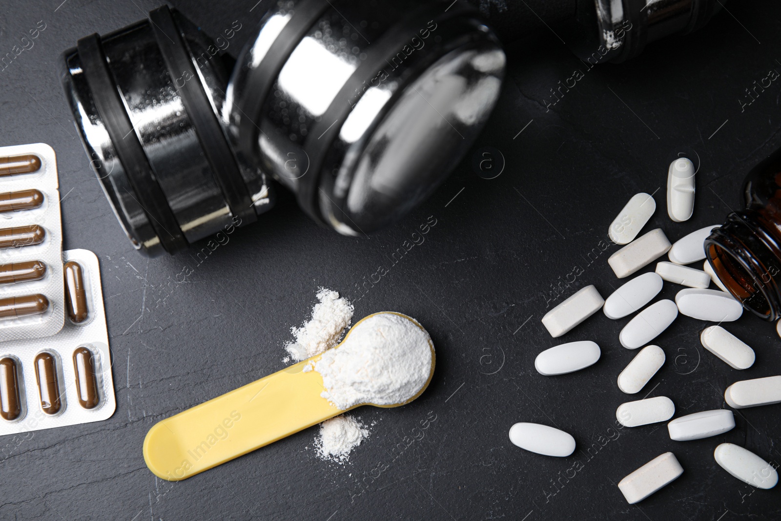 Photo of Pills, measuring scoop of amino acids powder and dumbbells on black table, flat lay