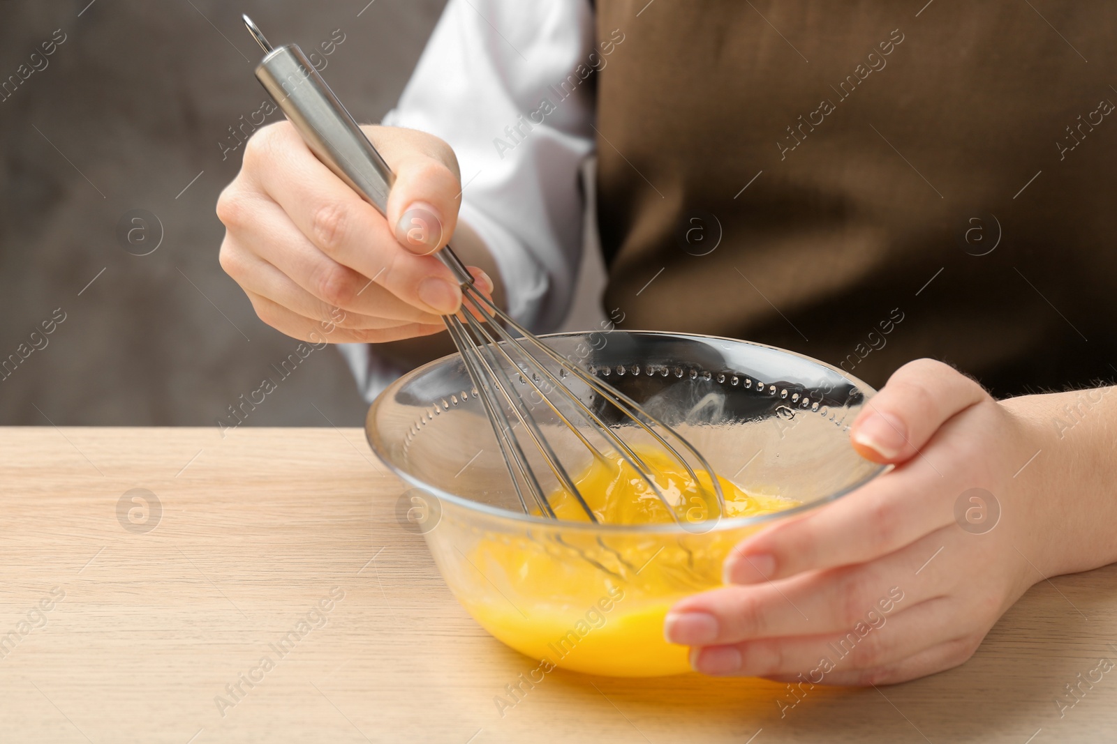 Photo of Woman whisking eggs in glass bowl at wooden table, closeup