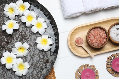 Photo of Bowl of water with flowers and different spa supplies on white wooden table, flat lay