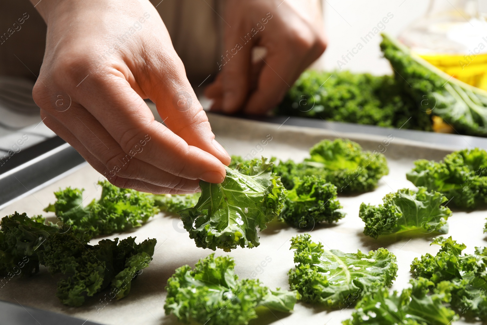 Photo of Woman preparing kale chips at table, closeup