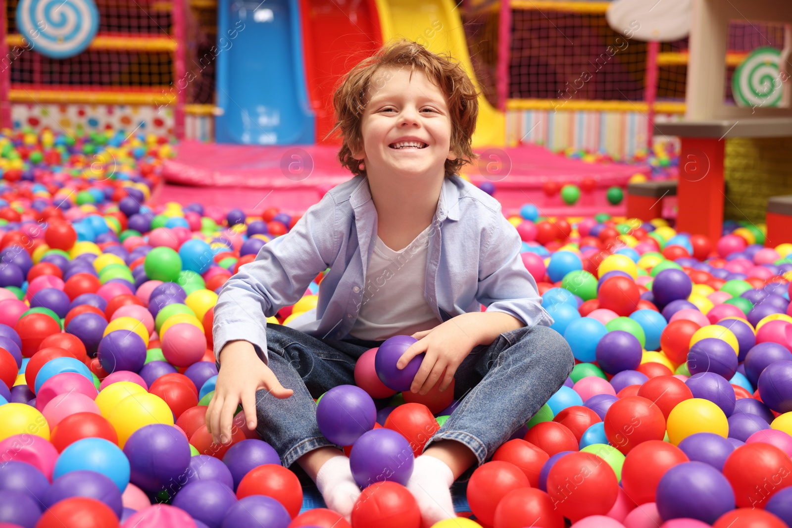 Photo of Happy little boy sitting on colorful balls in ball pit