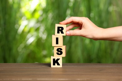 Photo of Woman stacking cubes with word Risk on wooden table, closeup