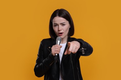 Beautiful young woman with microphone singing on yellow background