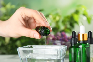 Woman dripping essential oil into bowl on table, closeup