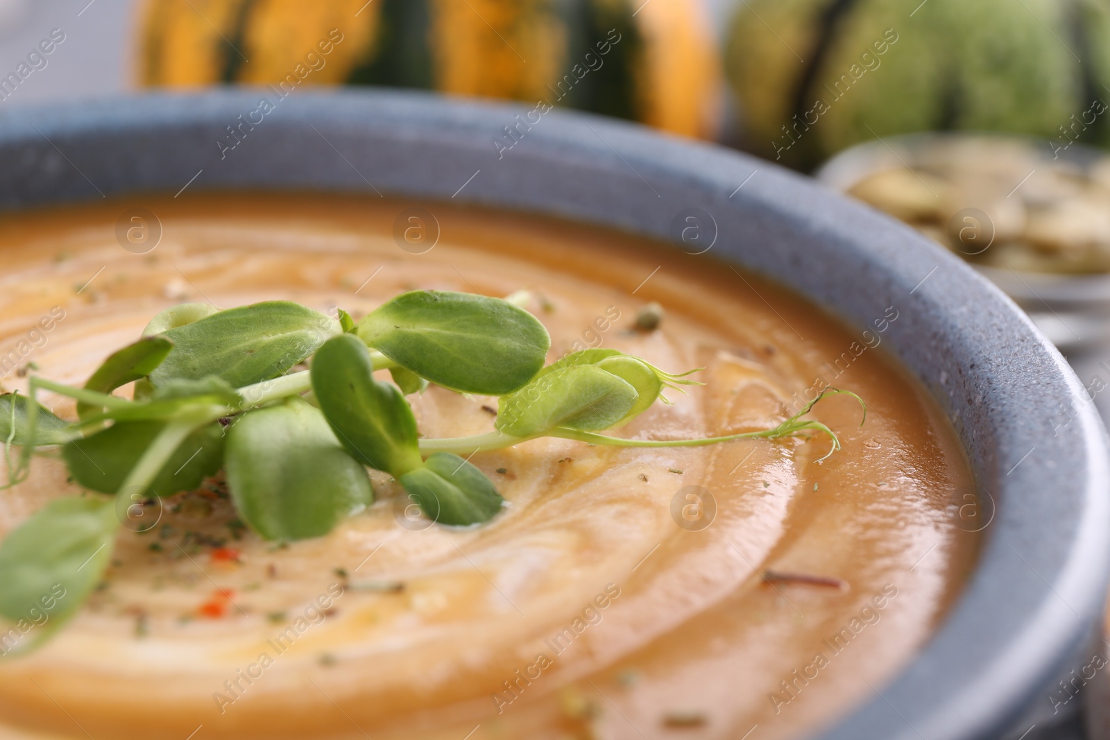 Photo of Tasty pumpkin soup with microgreens in bowl on table, closeup