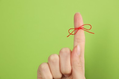 Photo of Woman showing index finger with tied red bow as reminder on light green background, closeup
