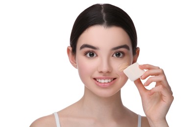 Photo of Teenage girl applying foundation on face with makeup sponge against white background