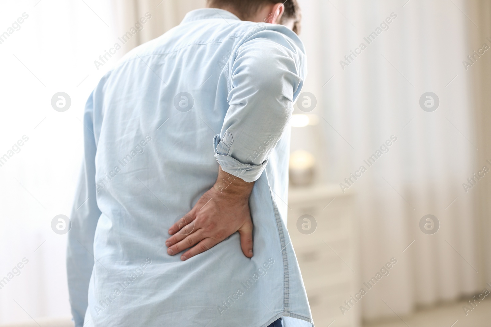 Photo of Man suffering from back pain at home, closeup. Bad posture problem