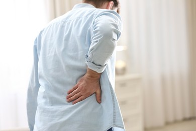 Photo of Man suffering from back pain at home, closeup. Bad posture problem