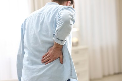 Man suffering from back pain at home, closeup. Bad posture problem