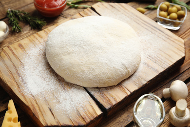 Photo of Dough and fresh ingredients for pizza on wooden table, closeup