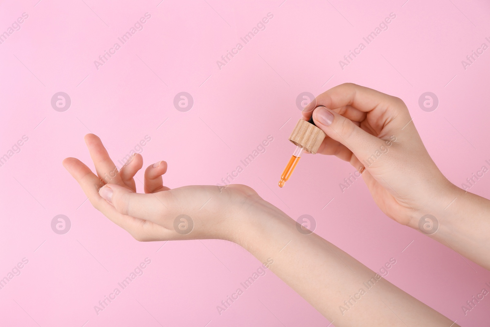 Photo of Woman applying essential oil onto wrist against pink background, closeup