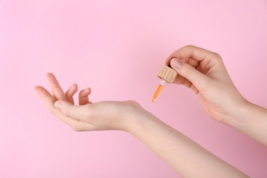 Photo of Woman applying essential oil onto wrist against pink background, closeup