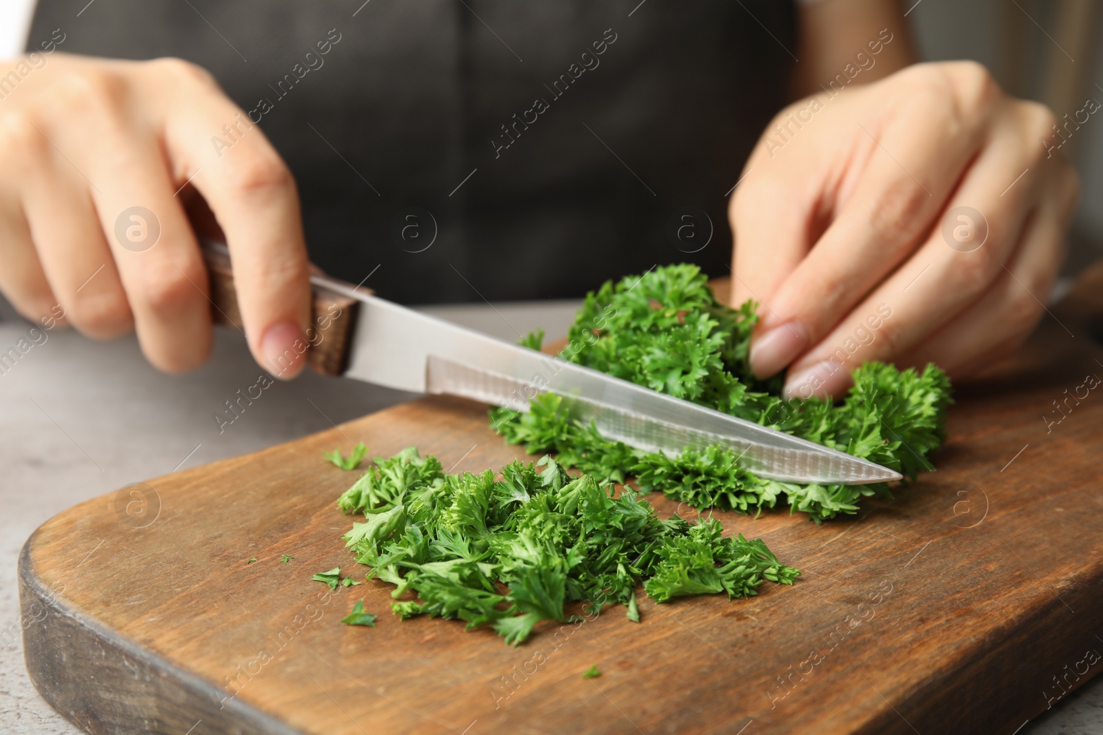 Photo of Woman cutting fresh green parsley on wooden board, closeup