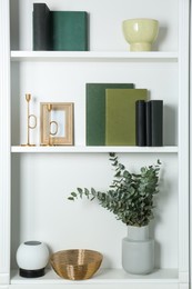 Photo of White shelves with books, eucalyptus and different decor indoors. Interior design