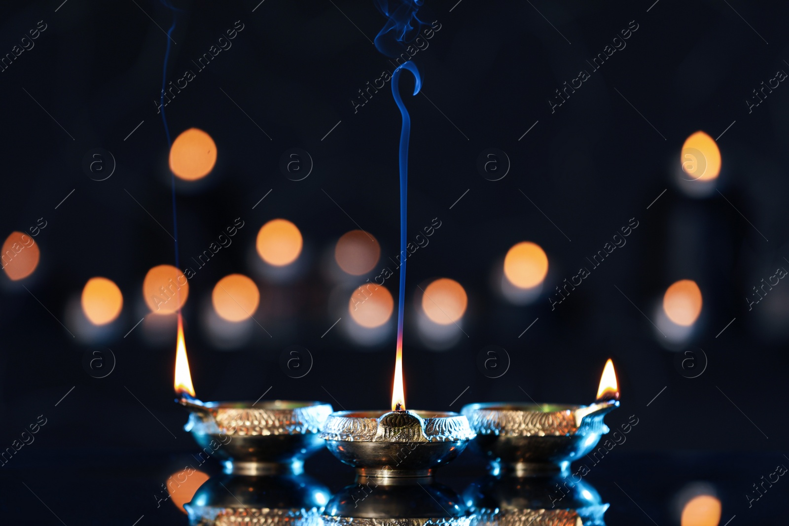 Photo of Lit diyas on table against blurred lights. Diwali lamps