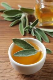 Photo of Bowl of essential sage oil and leaves on wooden table
