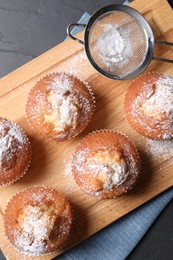 Photo of Delicious sweet muffins and sieve on black textured table, top view