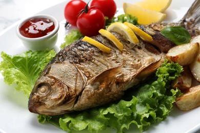 Photo of Tasty homemade roasted crucian carp with garnish on plate, closeup. River fish