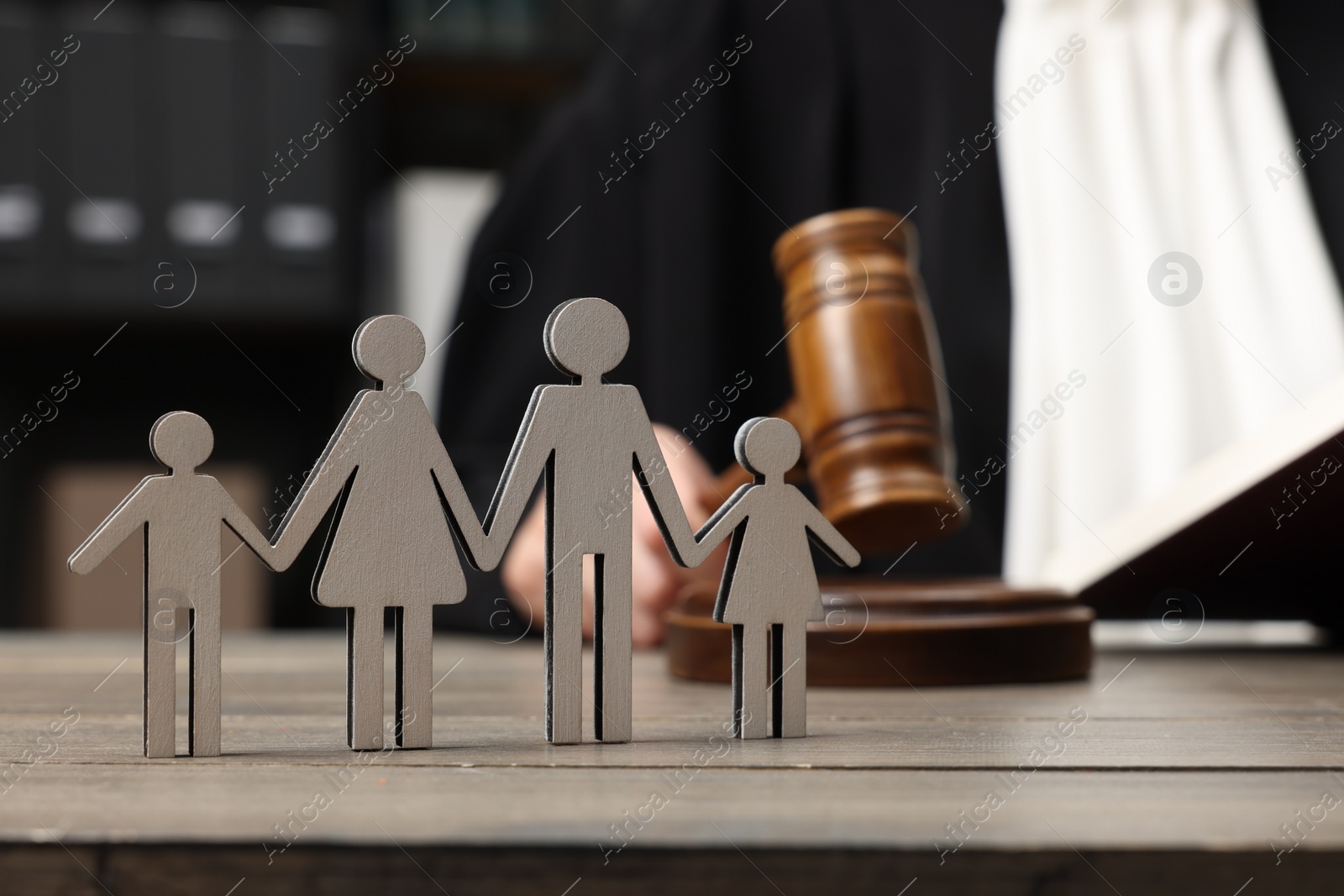 Photo of Family law. Judge with gavel sitting at wooden table, focus on figure of parents and children