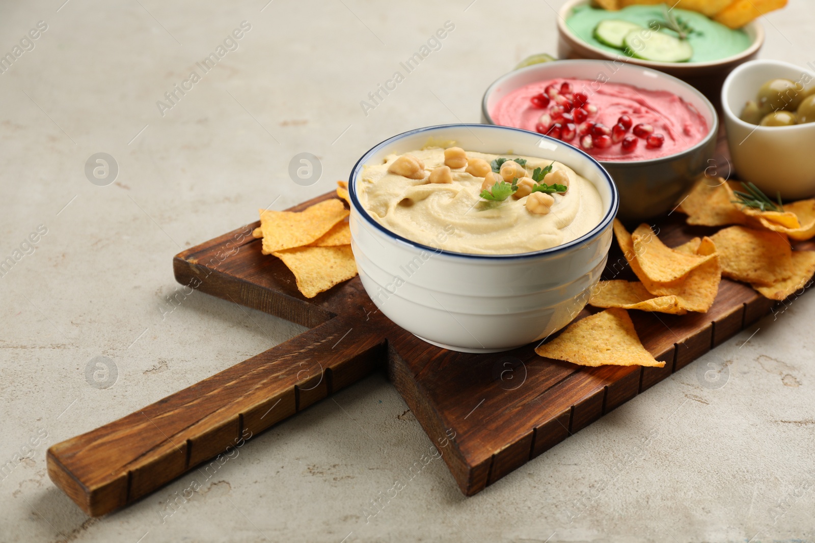 Photo of Different kinds of tasty hummus served with nachos on light table