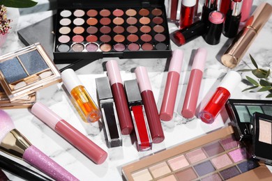 Bright lip glosses among different cosmetic products on white dressing table