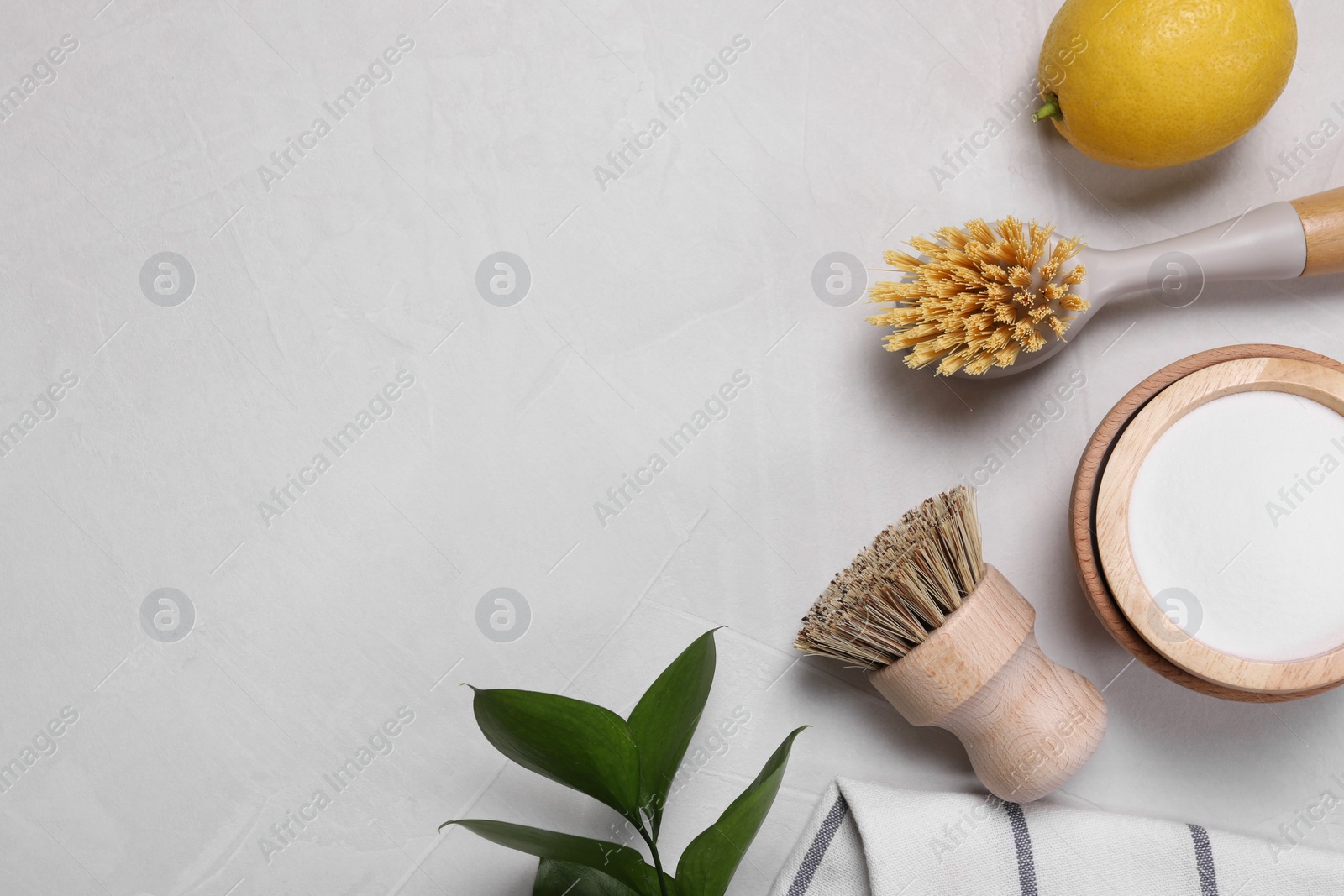 Photo of Cleaning brushes, baking soda, lemon and green leaves on white table, flat lay. Space for text