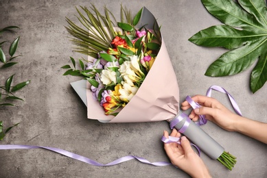 Photo of Woman making beautiful bouquet of freesia flowers on grey background