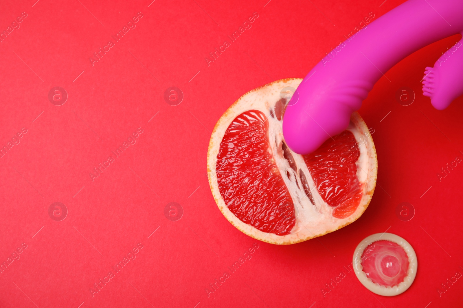 Photo of Half of grapefruit, purple vibrator and condom on red background, flat lay with space for text. Sex concept