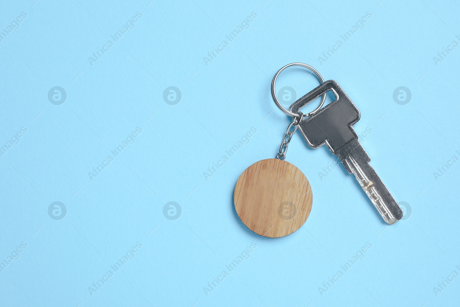 Photo of Key with wooden keychain in shape of smiley face on light blue background, top view. Space for text