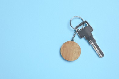 Photo of Key with wooden keychain in shape of smiley face on light blue background, top view. Space for text