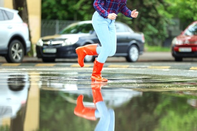 Photo of Woman with red rubber boots running in puddle, closeup. Rainy weather