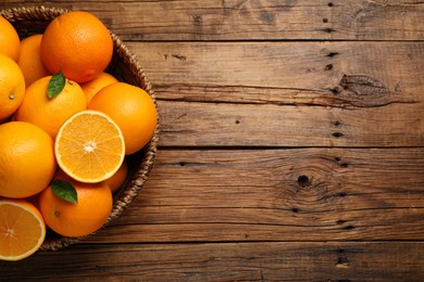 Photo of Many ripe oranges and green leaves on wooden table, top view. Space for text