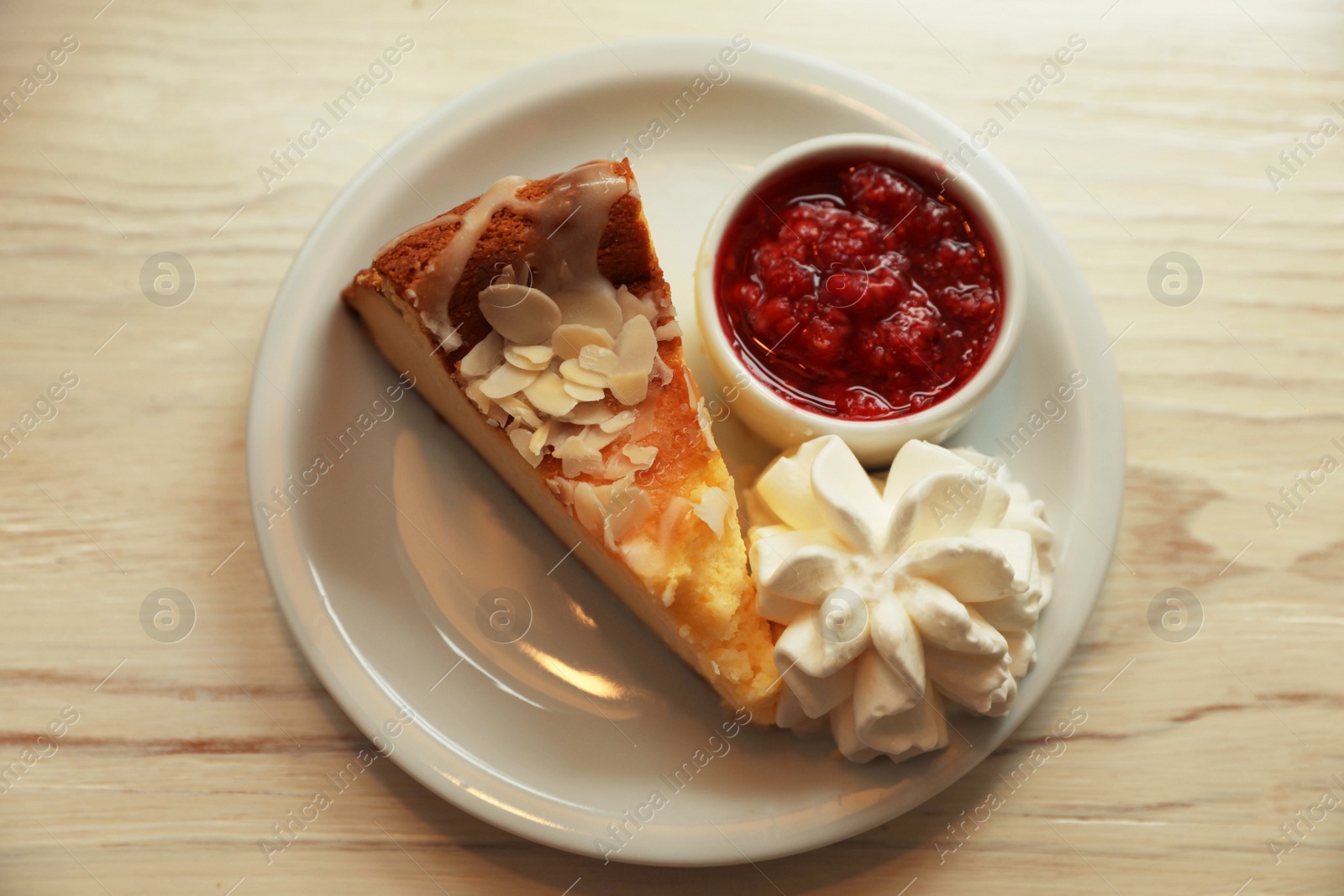 Photo of Piece of delicious cake with whipped cream and jam on white wooden table, top view