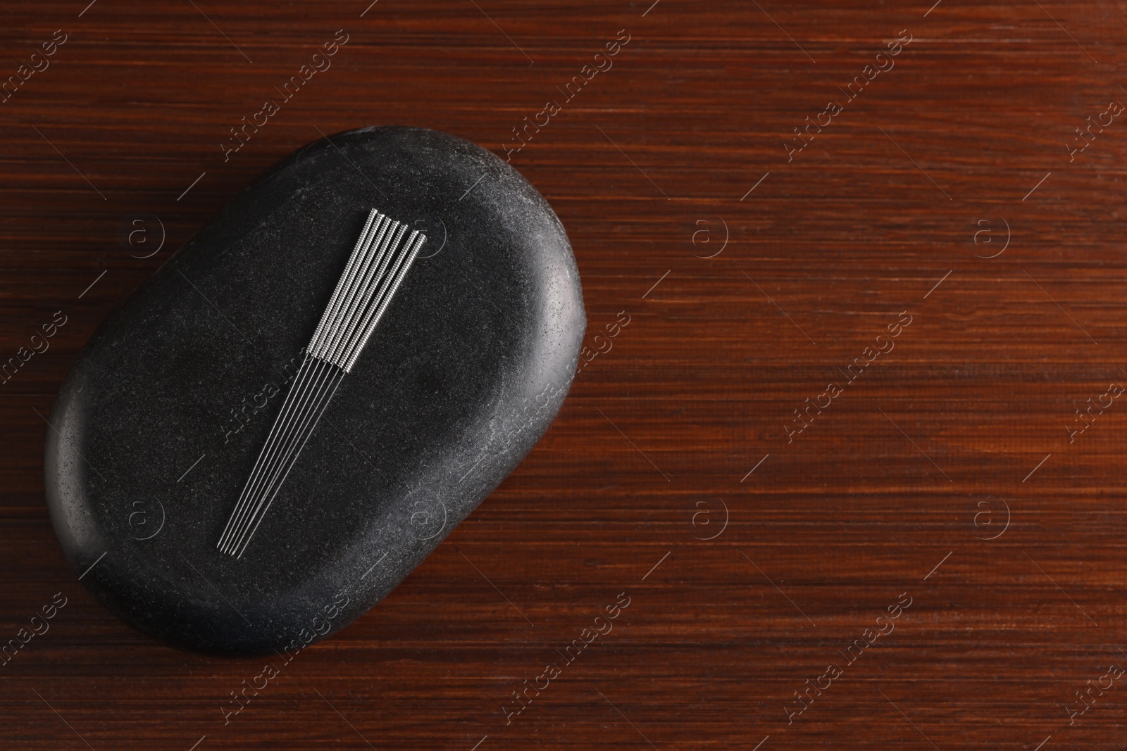 Photo of Acupuncture needles and spa stone on wooden table, top view. Space for text