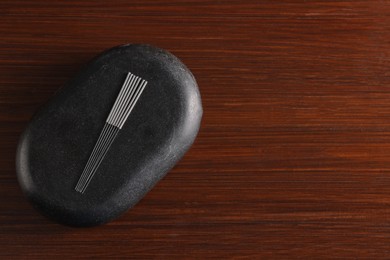 Photo of Acupuncture needles and spa stone on wooden table, top view. Space for text