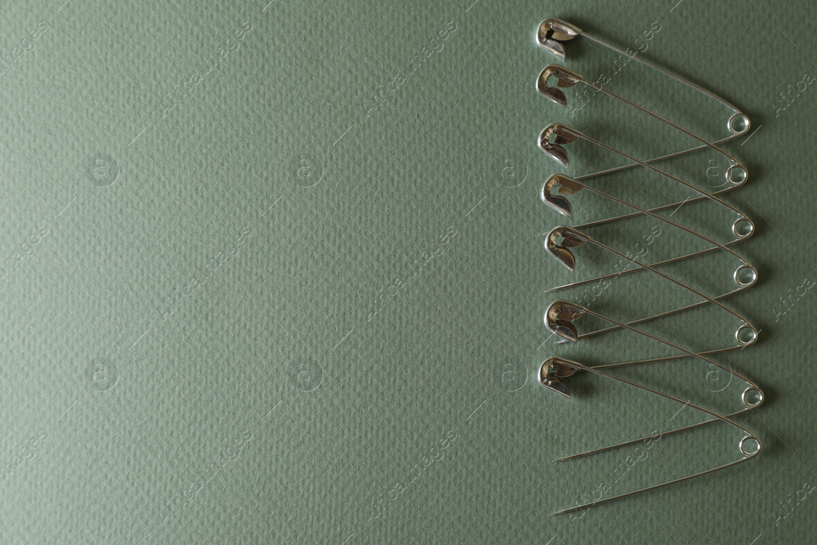 Photo of Many safety pins on green background, flat lay. Space for text