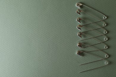 Photo of Many safety pins on green background, flat lay. Space for text