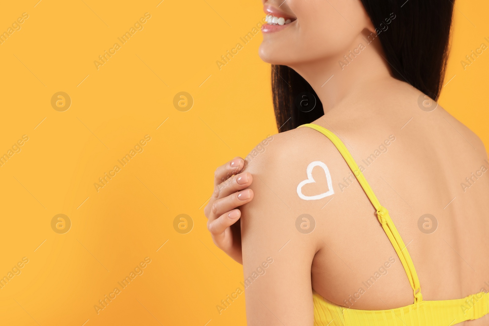 Photo of Young woman with heart drawn with sunscreen against orange background, closeup. Space for text