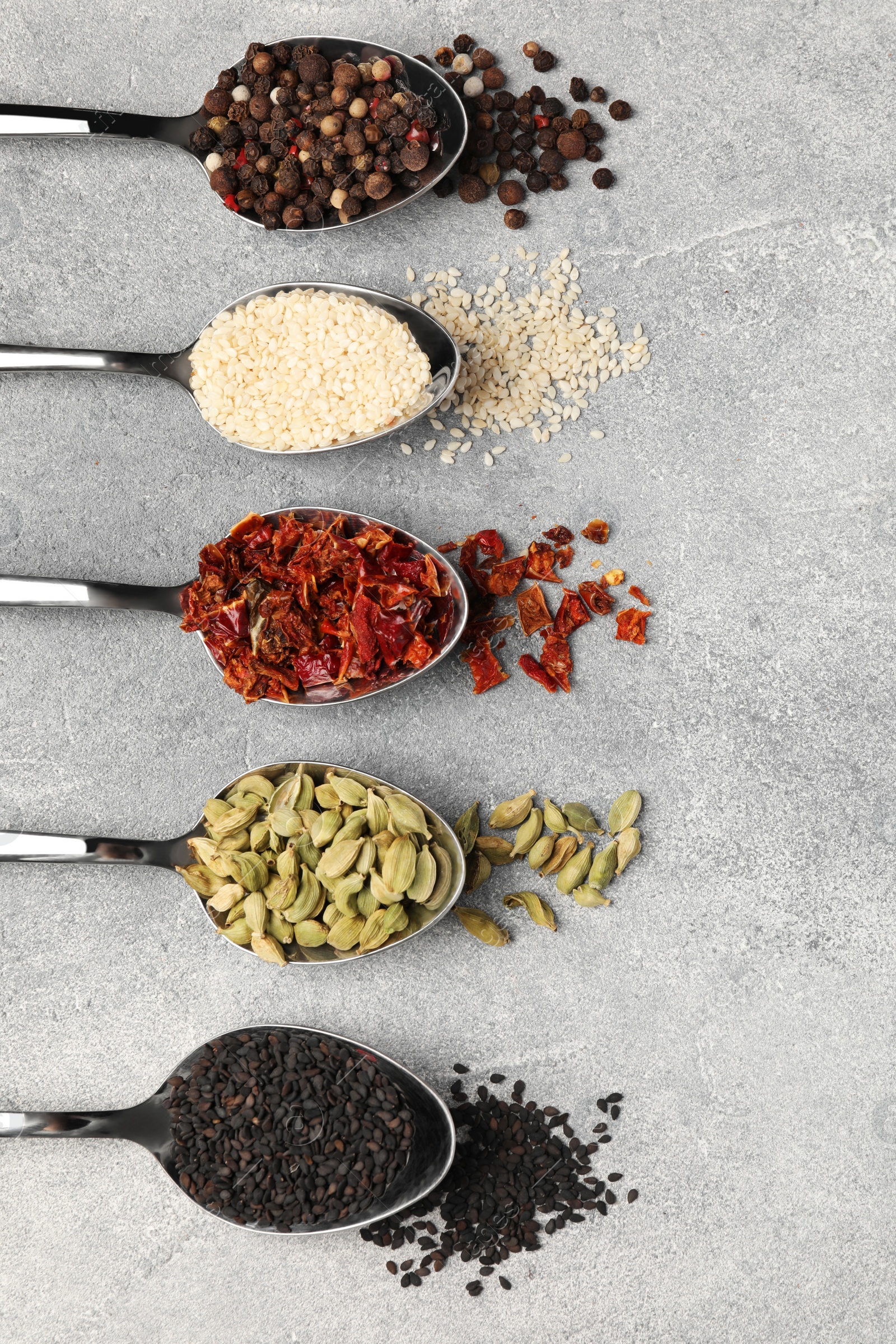 Photo of Metal spoons with different spices on light grey table, flat lay