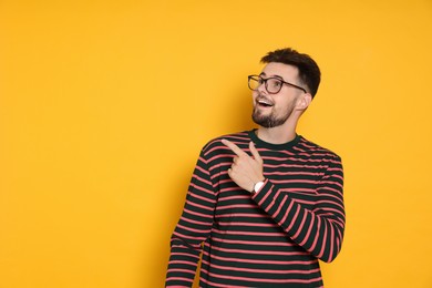 Handsome man in striped sweatshirt pointing at something on yellow background, space for text
