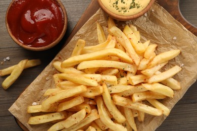 Delicious french fries served with sauces on wooden table, flat lay