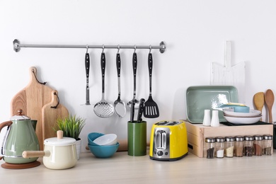 Set of clean cookware, dishes, utensils and appliances on table at white wall
