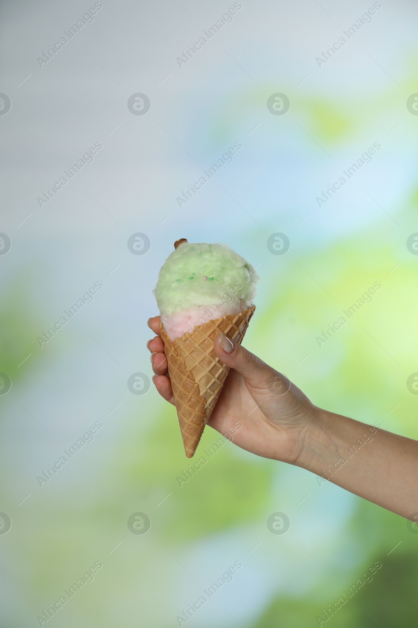 Photo of Woman holding waffle cone with cotton candy on blurred background, closeup