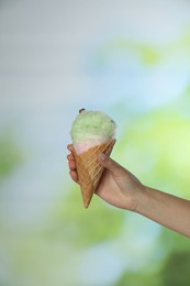 Woman holding waffle cone with cotton candy on blurred background, closeup