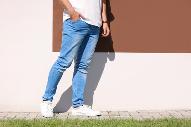 Photo of Young hipster man in stylish jeans posing near color wall