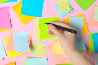 Woman writing on sticky note against pink background, top view